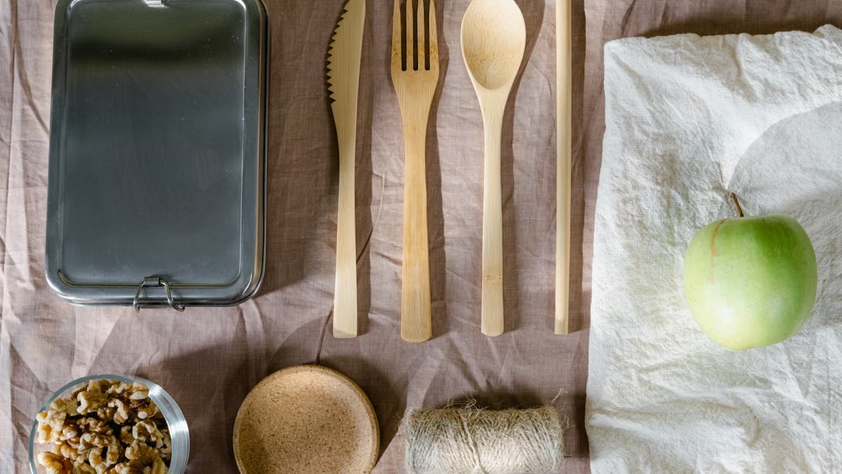 Sustainable flat lay arrangement with wooden utensils, green apple, and lunch box.